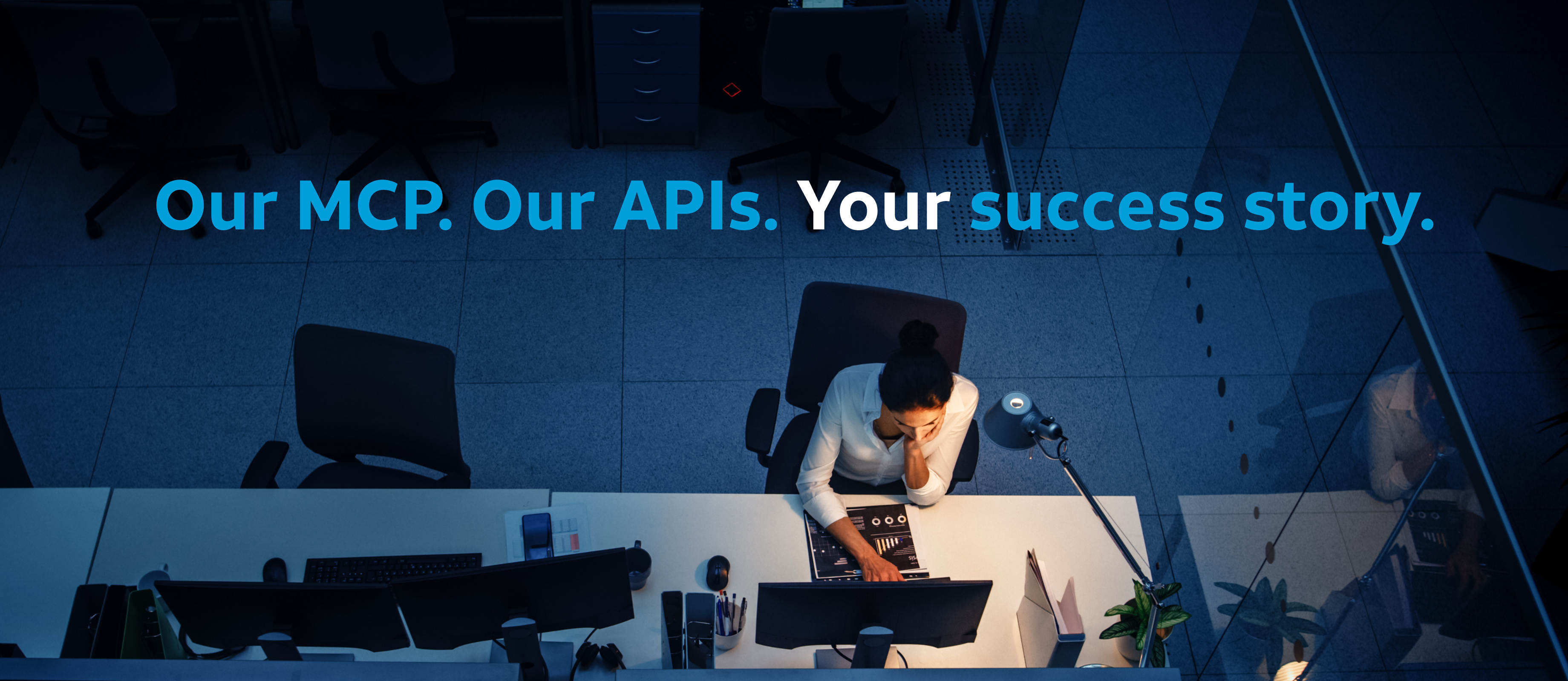 Woman on a computer in a dark room. Lit desk, dark blue background. Text reads "Our MCP. Our APIs. Your success story"